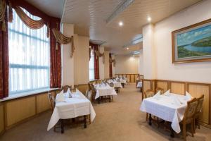 un restaurante con mesas y sillas blancas y ventanas en Dacia Hotel, en Chişinău
