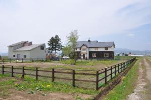 a house in a field next to a fence at Gufo no Mori Kamifurano in Kami-furano