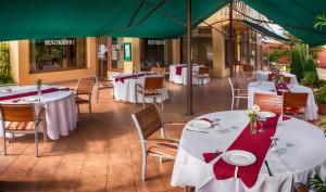 un restaurante con mesas y sillas blancas y sombrillas verdes en Csipke Hotel en Kiskunhalas