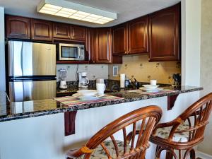 une cuisine avec des armoires en bois et un comptoir avec deux chaises dans l'établissement Regatta Beach Club C713, à Clearwater Beach