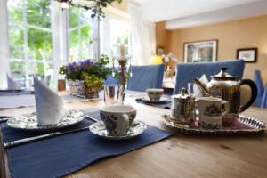 una mesa de madera con tazas de té y platos. en Das kleine Hotel am Park Garni en Bispingen