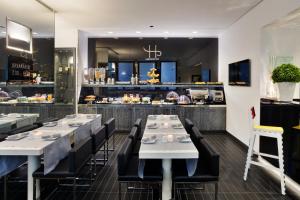 a restaurant with white tables and black chairs and a kitchen at LHP Hotel Napoleon in Milan