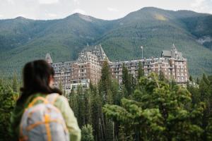 a woman with a backpack looking at a building in the mountains at Fairmont Banff Springs in Banff