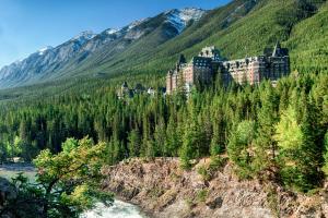 a castle on a hill with trees and a river at Fairmont Banff Springs in Banff