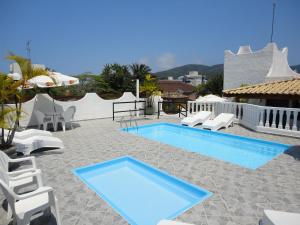 a swimming pool with white chairs and a blue poolvisor at Pousada Torre Del Mar in Ubatuba