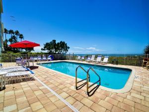 a swimming pool with chairs and an umbrella and the ocean at Beachside Hideout Unit K in Clearwater Beach