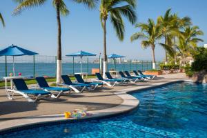 a pool with chairs and palm trees and the ocean at Hotel El Pescador in Puerto Vallarta