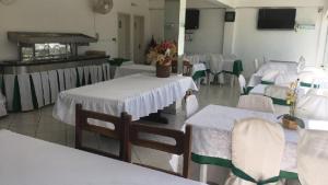 Una habitación con mesas y sillas blancas con flores. en Hotel Kika, en São Gabriel