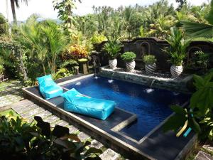 a swimming pool with two blue chairs in a garden at Villa Gede Private Guest House in Selemadeg
