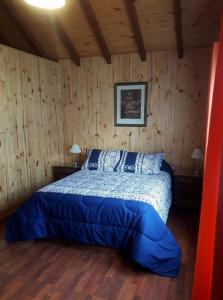 1 dormitorio con 1 cama con sábanas azules y paredes de madera en El hostel secreto en Lago Puelo