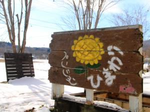 um sinal de madeira com um girassol pintado na neve em Pension Himawari em Iizuna