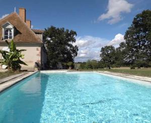 una piscina de agua azul frente a una casa en Maison du Fermier, en Épineuil-le-Fleuriel