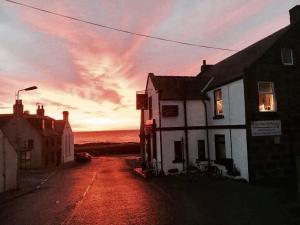 a street with a house and the ocean at sunset at Anchor Hotel in Johnshaven