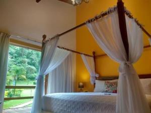 a bedroom with a canopy bed and a window at Pousada Tucano Do Cuiabá in Itaipava