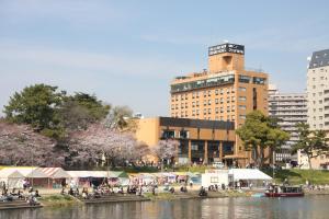 un grupo de personas sentadas junto a un río con edificios en Okazaki New Grand Hotel, en Okazaki