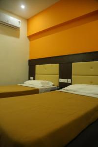 two beds in a room with orange walls at Hotel Sabareesh Plaza in Madurai