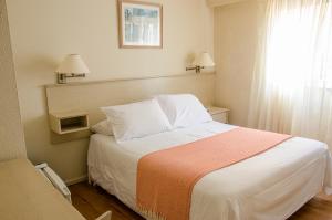 1 dormitorio con 1 cama grande con sábanas blancas y ventana en Hotel Sunset Beach, en Punta del Este