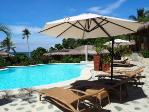 a swimming pool with chairs and an umbrella next to it at Magic Oceans Dive Resort in Anda