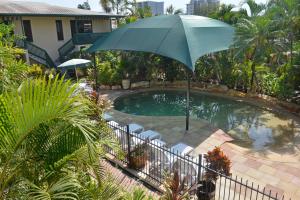 an umbrella and chairs next to a swimming pool at City Gardens Apartments in Darwin
