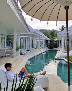 a man laying on a couch next to a swimming pool at Harmony Villas in Kuta Lombok