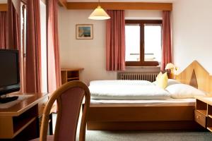 a bedroom with a bed and a desk and a television at Garni Renzler in Rasun di Sopra