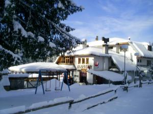 a building with snow on the ground in front of it at Family Hotel Markony in Pamporovo