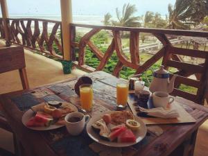a wooden table with a plate of food and orange juice at White Sands in Paje