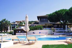 a swimming pool with an umbrella and chairs and a house at Hotel Porto Piccolo in Baja Sardinia