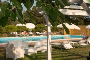 una piscina con sedie bianche e ombrelloni accanto a una piscina di Sicily Country House & Beach a Catania