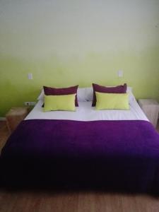 Cama grande con sábanas moradas y almohadas amarillas en Hosteria Ruphay en Tandil