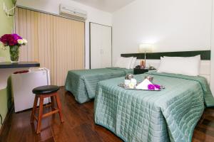 a hotel room with two beds and a stool at Hotel Minas Tower Leopoldina By Samba in Leopoldina