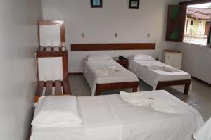 three beds in a room with white sheets at Pousada Do Bosque in Itajuípe
