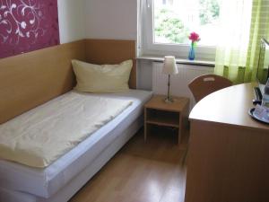ein kleines Bett in einem Zimmer mit einem Schreibtisch und einem Fenster in der Unterkunft Leuchtners an der Rennbahn in Iffezheim