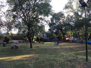 un parque con un parque infantil con un árbol y sillas en Robinson Apartamentos SOLO FAMILIAS en Villa Carlos Paz