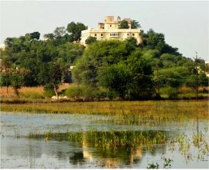 a house on top of a hill next to a body of water at Titardi Garh- 18th Century Castle Homestay in Udaipur