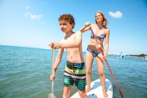Un ragazzo e una ragazza su una tavola da paddle in acqua di Golfo del Sole Hotel a Follonica