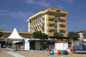 un grand bâtiment jaune avec une aire de jeux en face dans l'établissement Appartamenti Montmartre, à Rimini