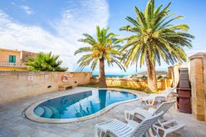 a swimming pool with white chairs and palm trees at Il-Palma Holiday Farmhouse with Sunny Private Pool in Island of Gozo in Għarb