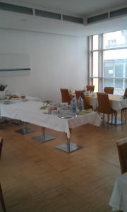 a dining room with white tables and chairs and windows at Hôtel Galerie in Greifswald