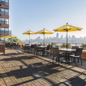 eine Reihe von Tischen und Stühlen mit gelben Sonnenschirmen in der Unterkunft Global Luxury Suites at Hoboken Waterfront in Hoboken