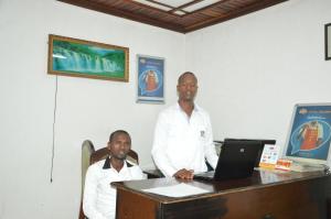 two men standing next to a desk with a laptop at Ubumwe Hotel in Gisenyi