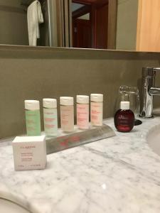 a bathroom counter with four bottles of moisturizers and a mirror at Pefaco Hotel Maya Maya in Brazzaville