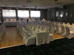 um salão de banquetes com mesas brancas e cadeiras brancas em Crookston Hotel em Glasgow