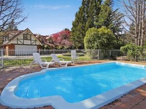 a blue swimming pool with two chairs and a house at Cedar Cottage - Tudor Village in Bright