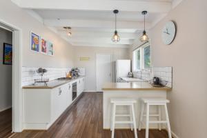 uma cozinha com armários brancos e um balcão com bancos em Blairgowrie Bella - light filled home with great deck em Blairgowrie