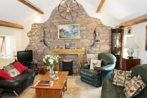 a living room with leather furniture and a stone wall at Piggery Cottage in Wigton