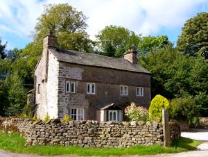 uma velha casa de pedra com uma cerca de pedra em frente em Fleshbeck Cottage em Barbon