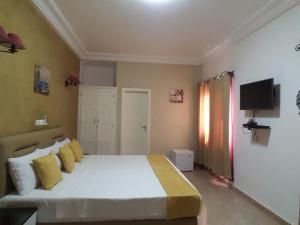 ein Schlafzimmer mit einem Bett mit gelben Kissen und einem TV in der Unterkunft Hôtel YABISSO in Lomé