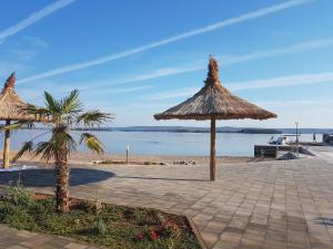 uma praia com dois guarda-sóis de palha e uma palmeira em Apartment Adria em Tkon