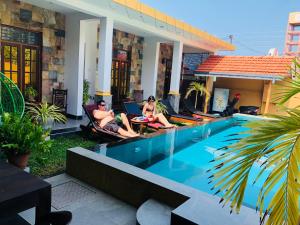twee personen in stoelen naast een zwembad bij St CLAIRE'S GREEN Negombo Hotel & Hostels in Negombo